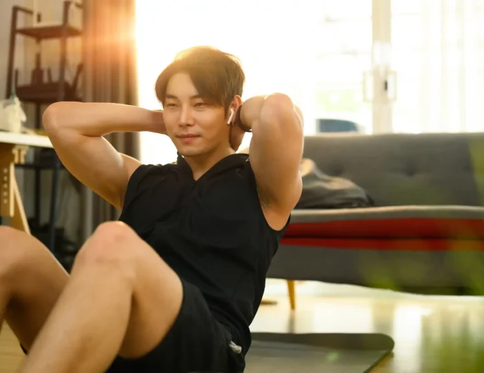 Strong asian man wearing sporty clothes doing sit up exercise during home workout.