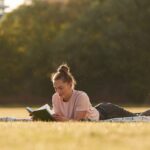 Woman is lying down on the summer field and reading a book