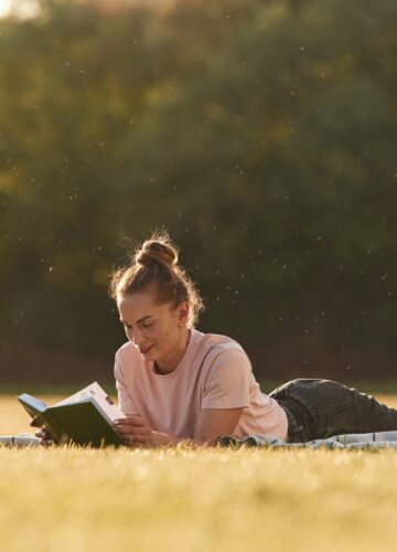 Woman is lying down on the summer field and reading a book