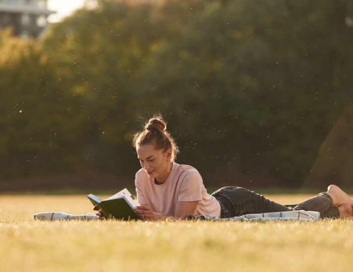 Woman is lying down on the summer field and reading a book