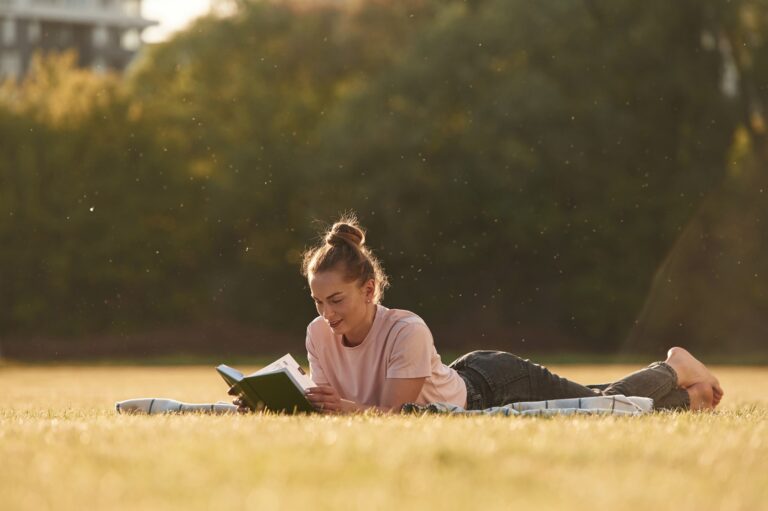 Woman is lying down on the summer field and reading a book